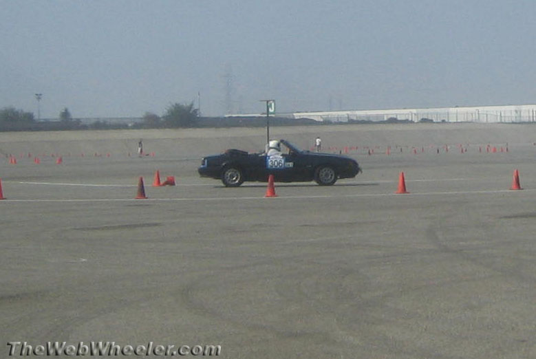 Black convertible Mustang with number 306 on door driving through a cone course.