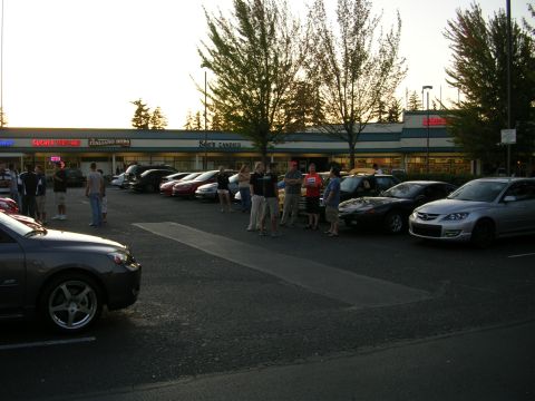 2007 Mazda 3 - A group of people gather around cars parked in a lot during a meet-up.