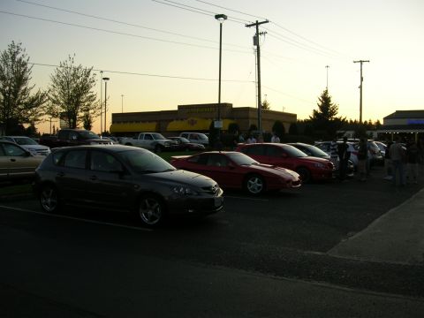 2007 Mazda 3 - A group of cars are parked in a lot during a meet, with a dark gray Mazda 3 in the foreground.