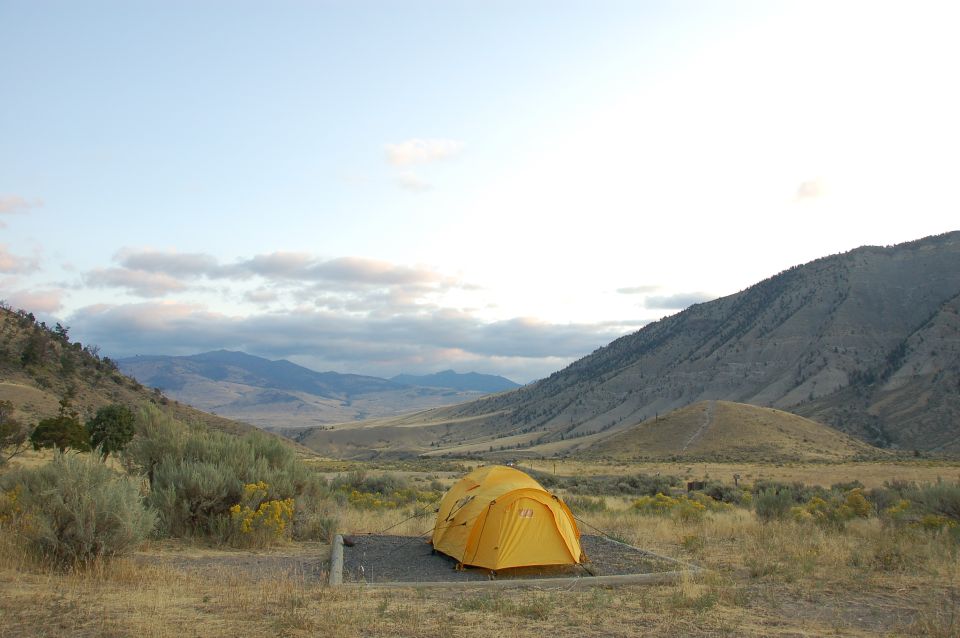 Yellow tent in a campsite with mountains and clouds.