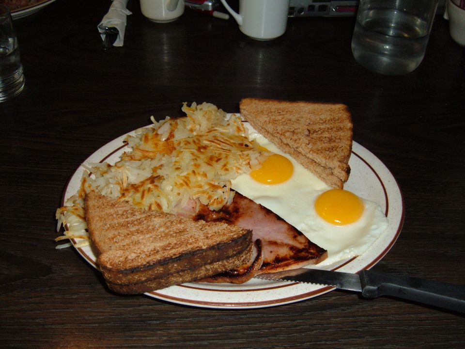 Breakfast plate with hash browns, fried eggs, ham, and toast on a wooden table.