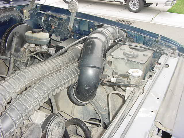 Engine bay of 1993 Ford Bronco showing black air intake tube, brake master cylinder and coolant reservoir