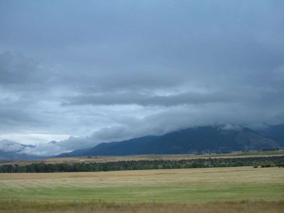 Landscape with mountains and fields under a cloudy sky.