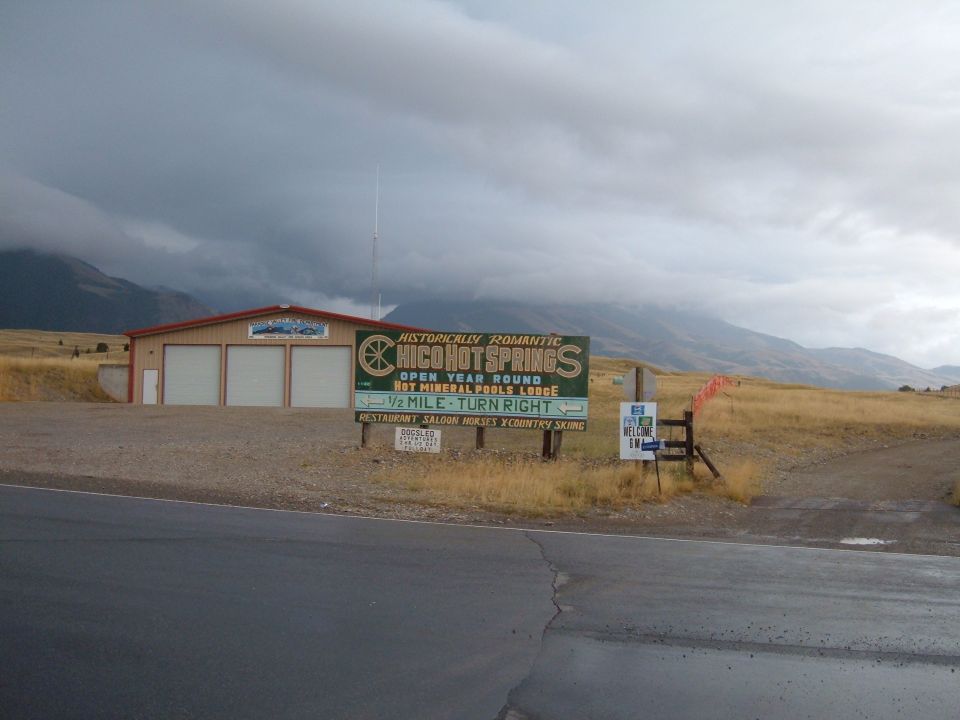Sign for Chico Hot Springs in front of a building and a mountain landscape.