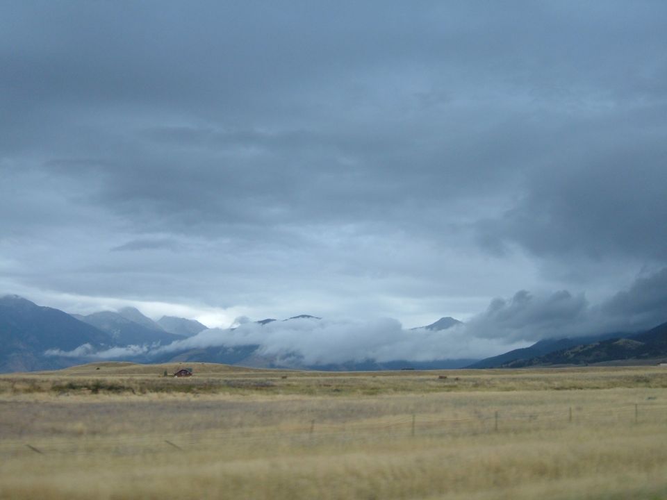 Dry grassland with mountains in the background under a cloudy sky.