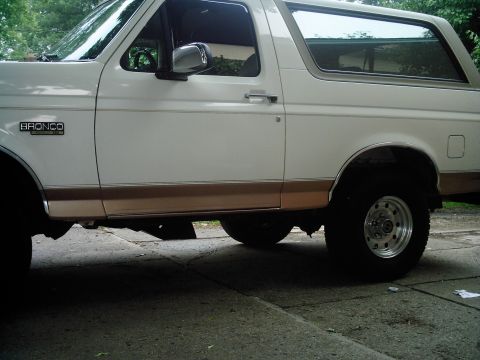 1995 Ford Bronco - Side view of a white Ford Bronco with tan lower trim and tinted windows.