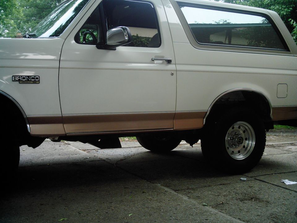 White and tan full-size Ford Bronco parked on concrete, low side view