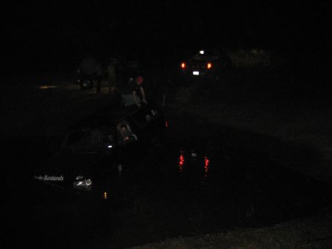 1995 Ford Bronco - Two vehicles are stuck in dark water at night, with people standing around them.