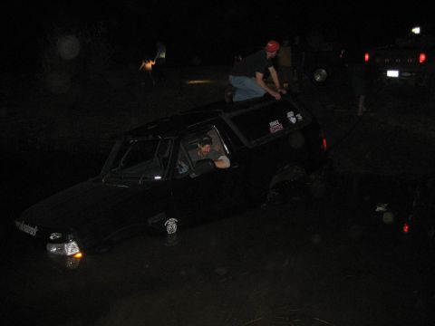 1995 Ford Bronco - A group of people are gathered around a black SUV that appears to be stuck in water at night.