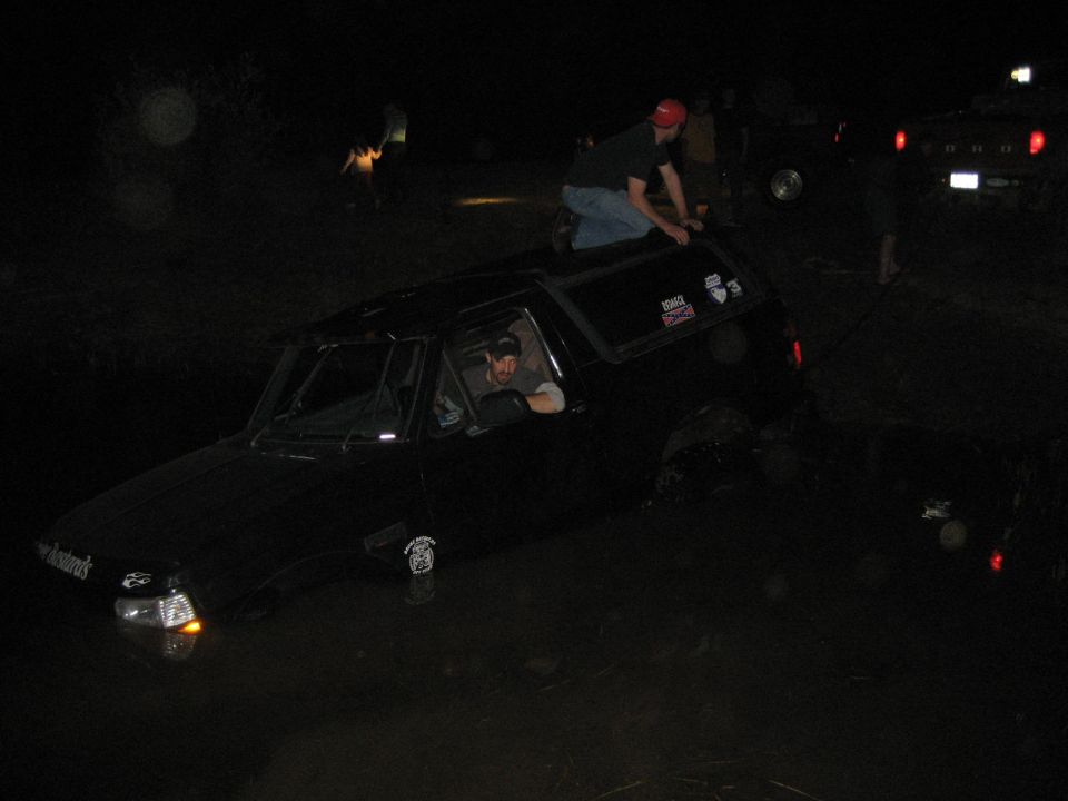 Black Ford Bronco stuck in water at night with driver leaning out and man on the roof