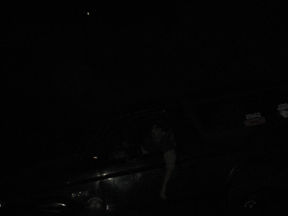 Very dark night photo of a person beside a vehicle, nearly all detail lost to underexposure