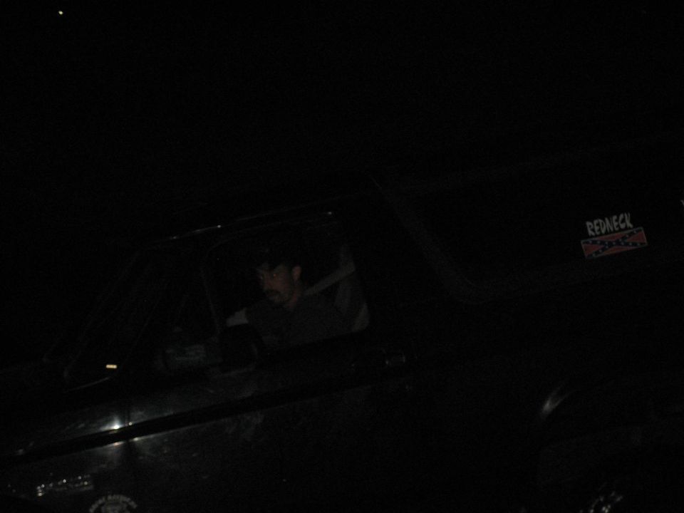 Dark nighttime side view of a full-size SUV with driver visible and quarter-window sticker