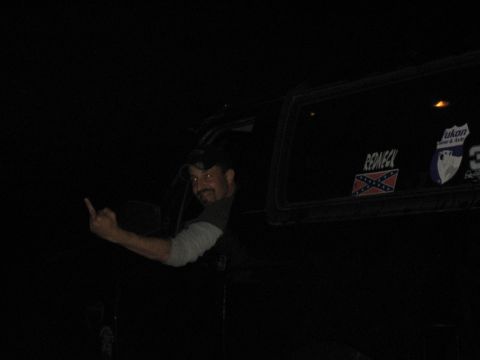 1995 Ford Bronco - A man leans out of a vehicle window at night, giving the middle finger while displaying several stickers on the glass.