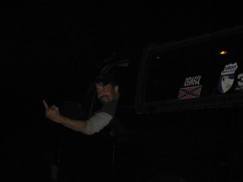 Man leaning from the window of a dark SUV at night with decals on the rear side glass