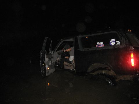 1995 Ford Bronco - A black SUV is partially submerged in dark water at night, with its driver's door open.