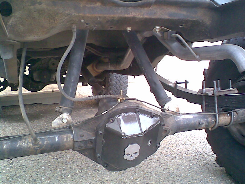 Rear axle assembly with custom differential cover a skull emblem. Leaf springs and shocks are visible