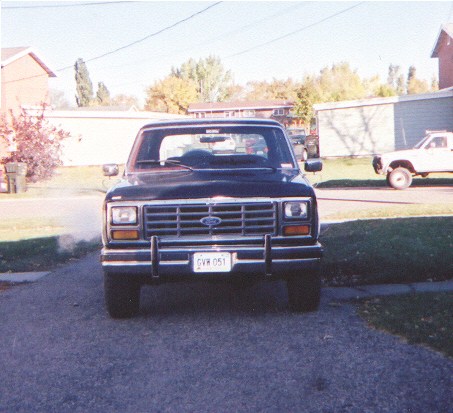 1986 Ford Bronco - Front view of a black 1986 Ford Bronco, showing its grille and license plate. Another vehicle is visible in the background.