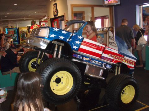1996 Ford Bronco - A child sits in a toy monster truck ride decorated with the American flag.