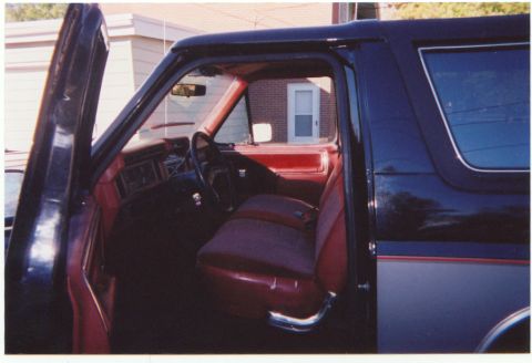 1986 Ford Bronco - The interior of a dark blue and gray Ford Bronco shows red seats and a partially visible dashboard.
