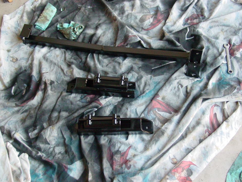 Black painted vehicle suspension components laid out on a patterned cloth with rags and a wrench