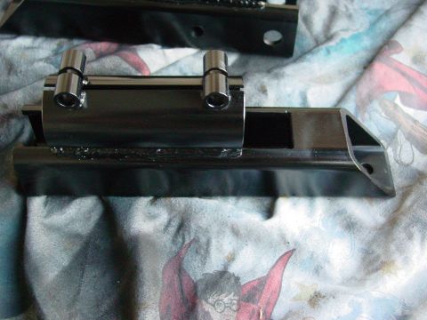 1979 Ford Bronco - A close-up view of a black metal suspension part with two silver pins attached.