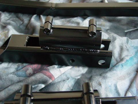 1979 Ford Bronco - Close-up of a black metal suspension component two cylindrical pins, resting on a patterned cloth surface.