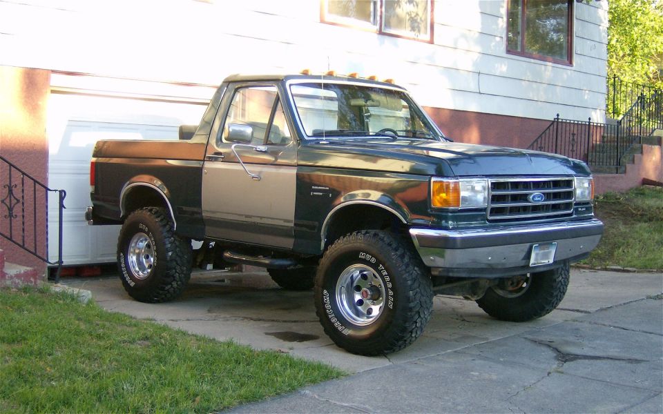 Ford Bronco parked in driveway, dark green and tan two-tone paint, lifted suspension, off-road tires