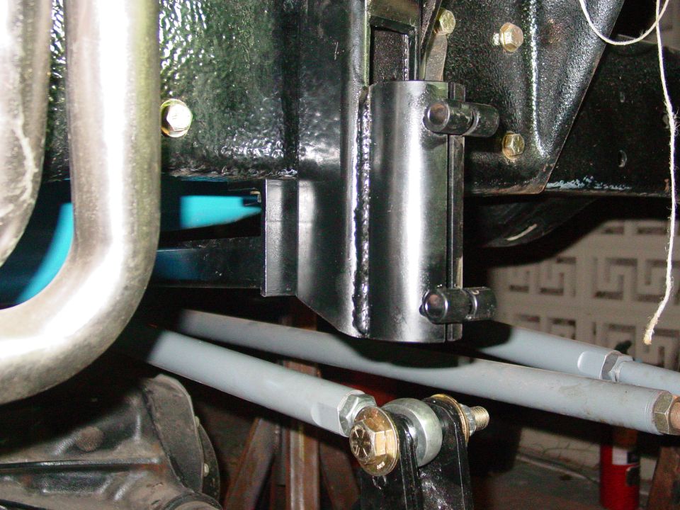 Close-up of vehicle suspension with gray tie rods and black metal brackets. Some welding visible