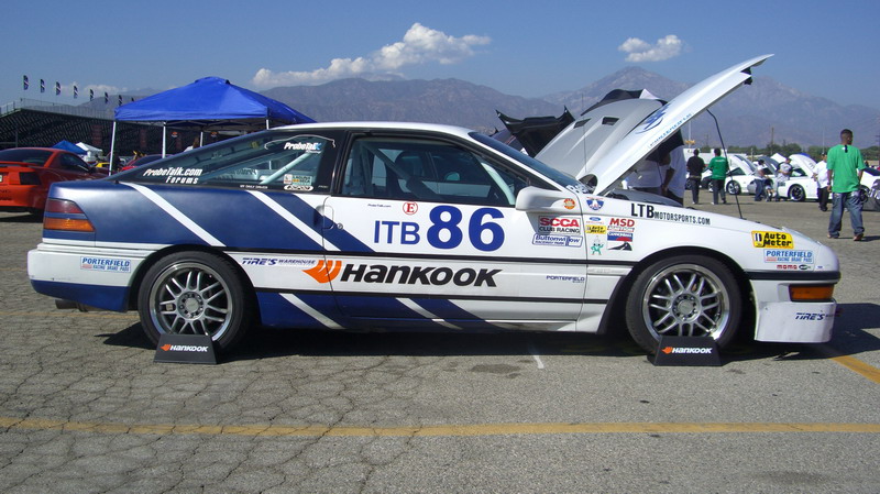 White and blue Ford Probe ITB 86 race car in side profile with hood open in the paddock