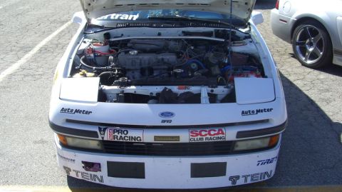 1990 Ford Probe - A white 1990 Ford Probe is parked with its hood open, revealing the engine and various racing stickers on the front.