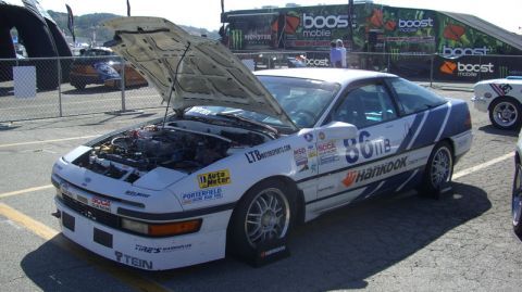 1990 Ford Probe - A white 1990 Ford Probe race car is displayed with its hood open, revealing the engine and numerous sponsor decals.