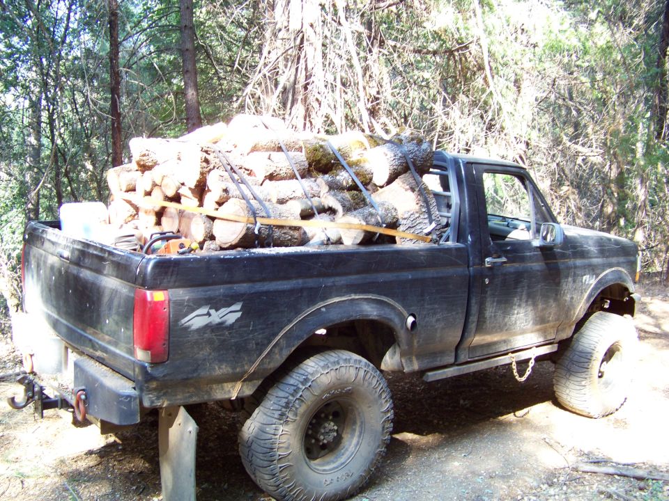 Black pickup truck with firewood and a chainsaw in the bed, parked on a dirt road