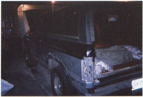 1986 Ford Bronco - The rear of a dark SUV is visible with the tailgate open, revealing cargo inside.