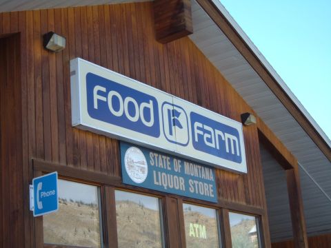 1998 BMW R1100GS ABS - A sign for Food Farm and State of Montana Liquor Store is mounted on a wood-paneled building.