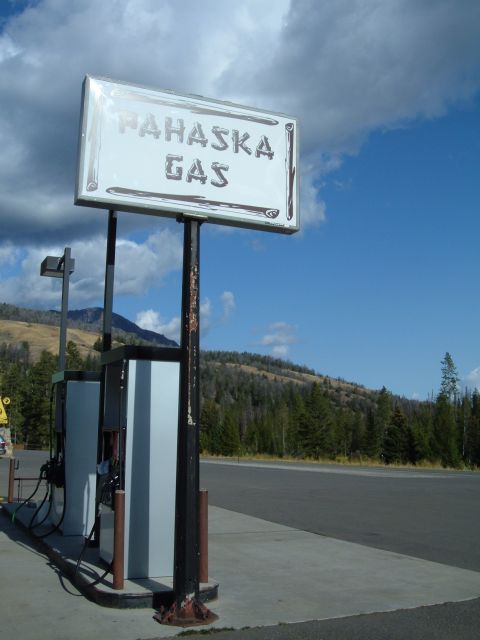 1998 BMW R1100GS ABS - A vintage gas station sign stands above weathered pumps, set against a backdrop of forested hills and a bright blue sky.