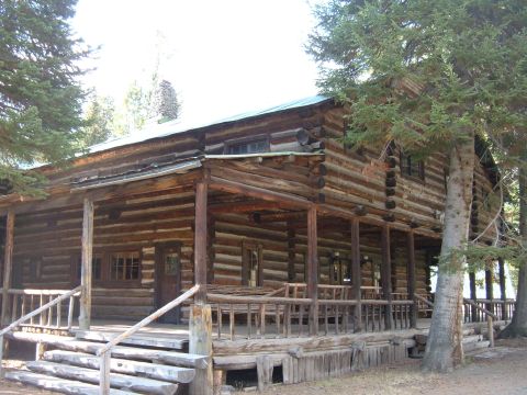 1998 BMW R1100GS ABS - A rustic log cabin with a wide porch and stone chimney stands among tall trees.
