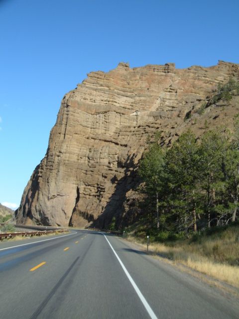 1998 BMW R1100GS ABS - A road winds through a landscape dominated by a massive, stratified rock cliff face.