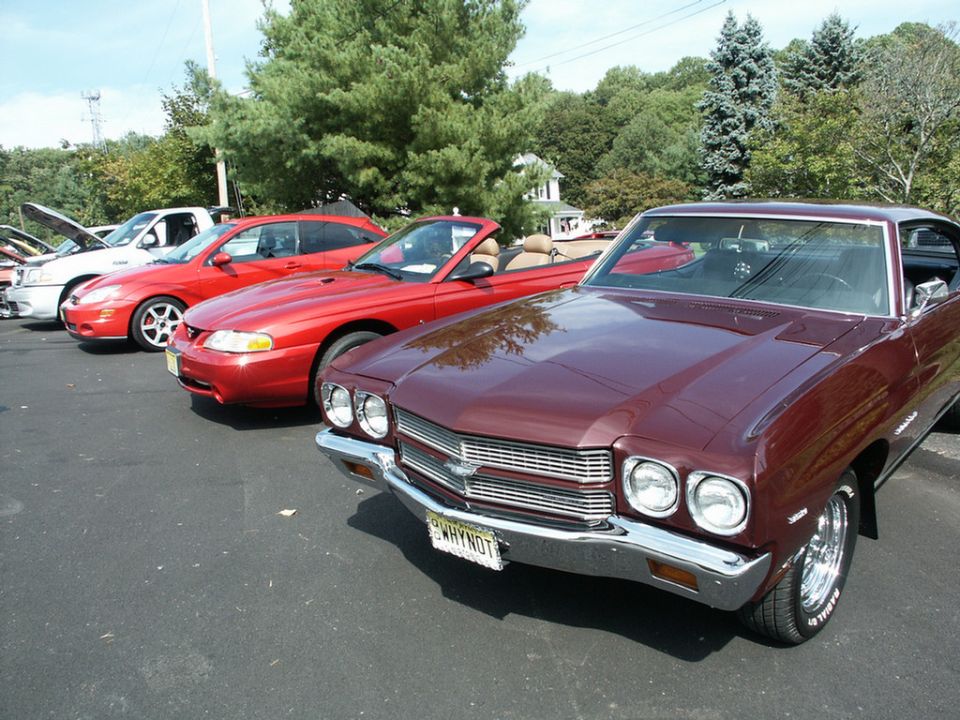 Maroon coupe with 'WHYNOT' license plate, red convertible, red coupe, and white pickup truck parked in a lot