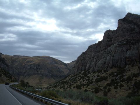 1998 BMW R1100GS ABS - A lone motorcycle travels a scenic highway through a dramatic mountain landscape under a cloudy sky.