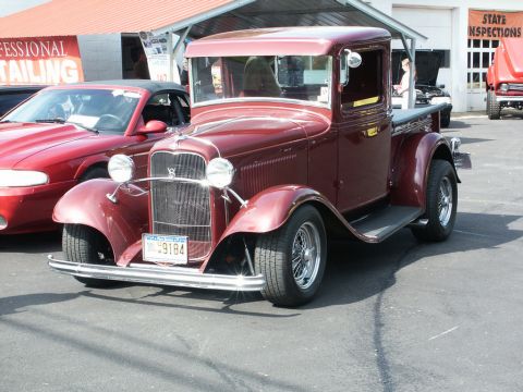 2001 Mercury Grand Marquis - A classic maroon pickup truck from the 1930s is displayed at a car show, with a modern red car visible to its left.