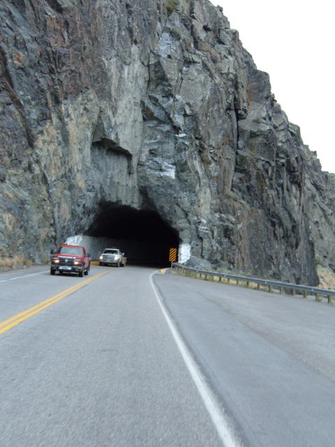 1998 BMW R1100GS ABS - Two pickup trucks drive on a road towards a tunnel entrance in a rocky mountainside.