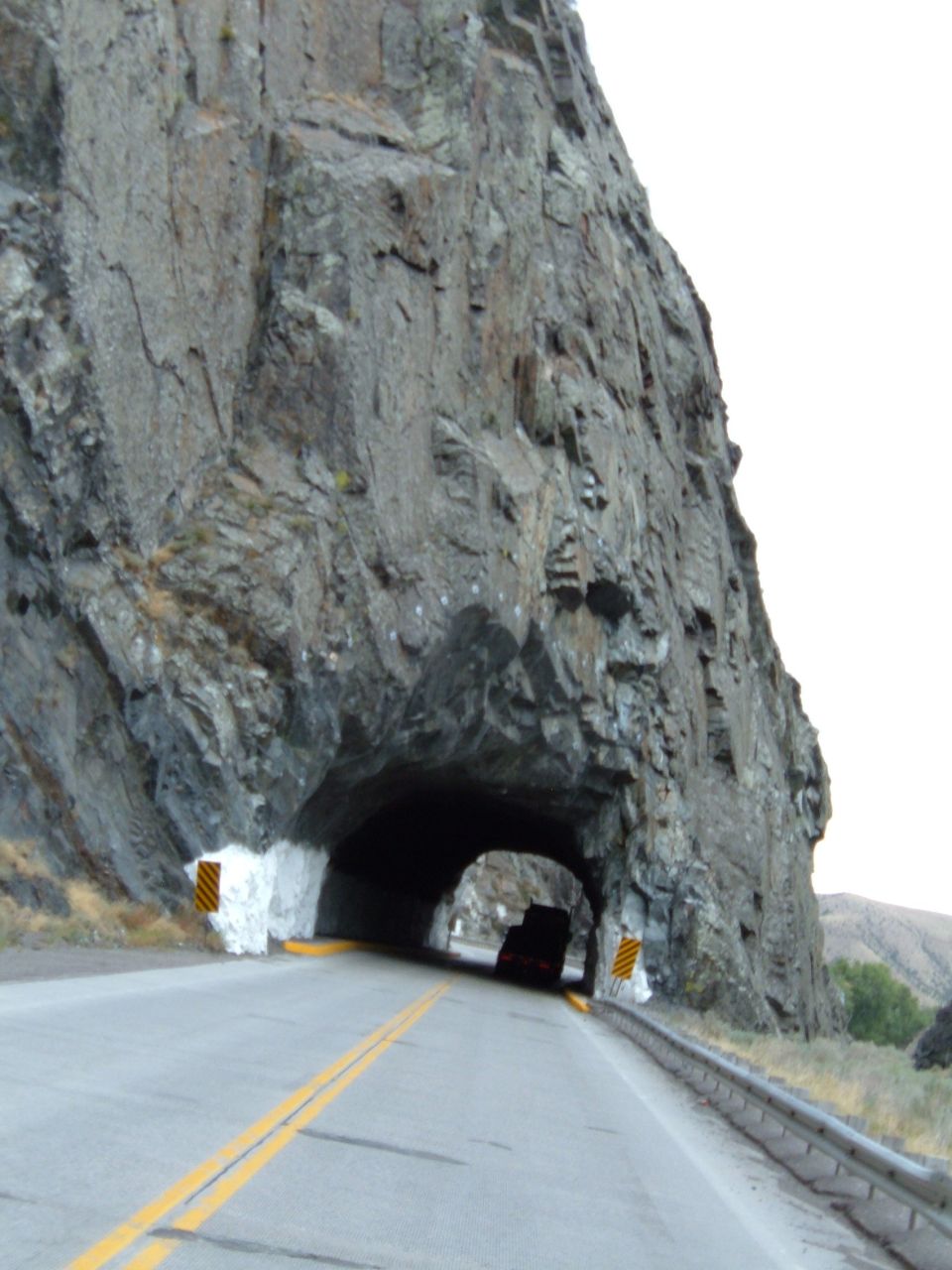 Driving towards a tunnel carved into a rocky cliff face, with a dark vehicle entering the tunnel