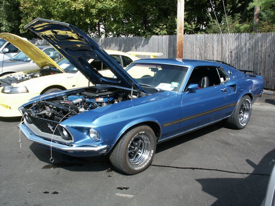 Blue 1969 Mustang Mach 1 with hood open, parked next to a yellow Mustang
