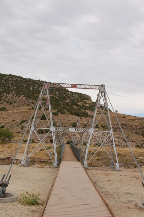 1998 BMW R1100GS ABS - A suspension bridge with a wooden walkway crosses a dry creek bed, leading towards a rocky, arid landscape.