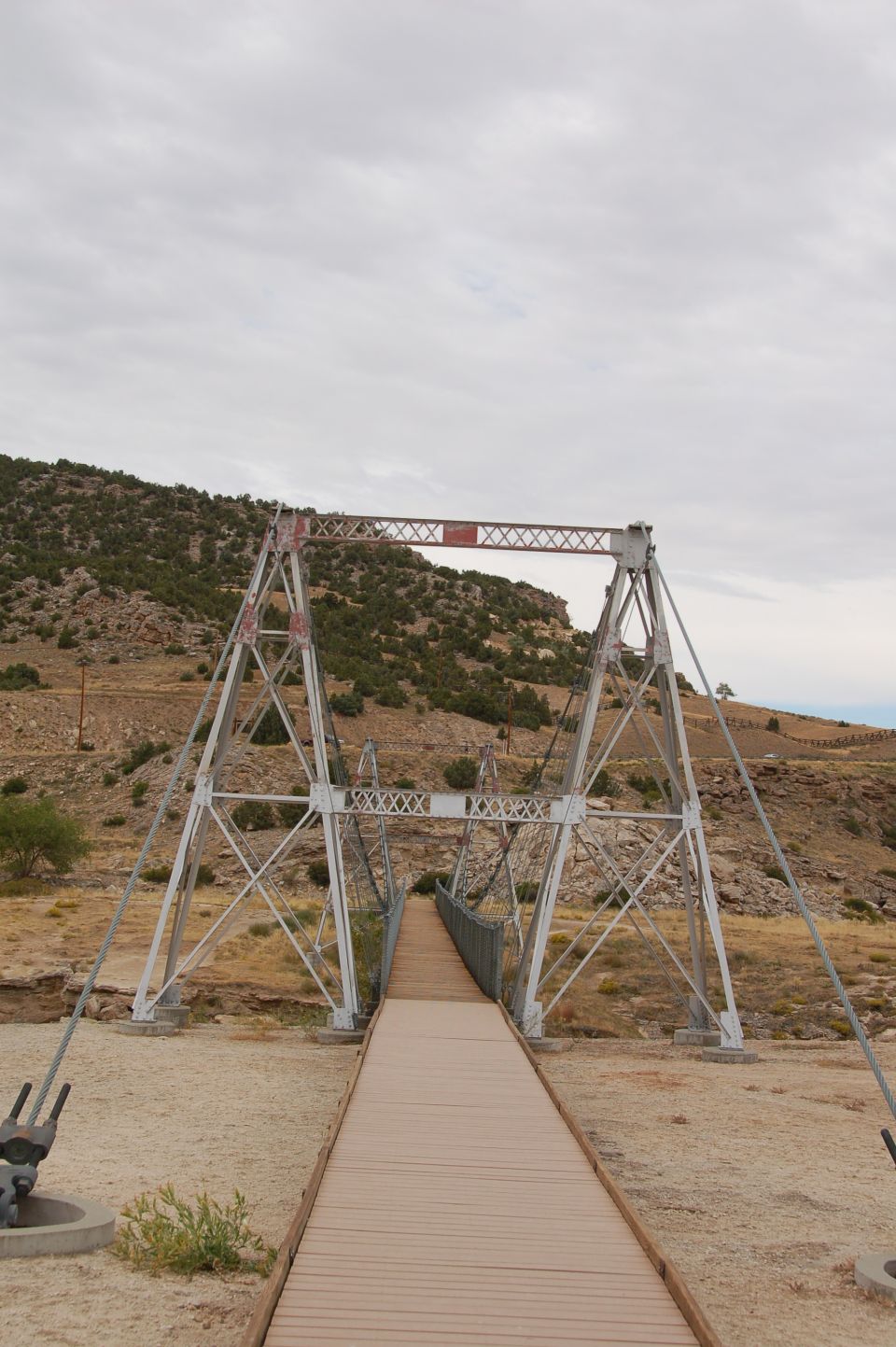 Suspension bridge with wooden walkway over dry creek bed, rocky hills in background