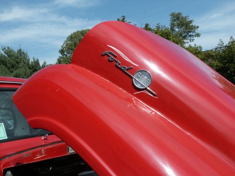 2001 Mercury Grand Marquis - A red Ford F-100 hood is open, revealing a chrome emblem and part of another vehicle.