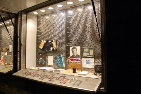1998 BMW R1100GS ABS - A display case exhibits a wall of names, a portrait, and artifacts, likely commemorating individuals.