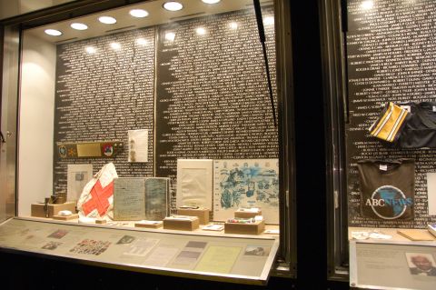1998 BMW R1100GS ABS - A museum display case features a wall of names, a flag, and various artifacts, including t-shirts with logos.
