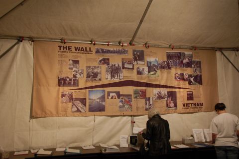 1998 BMW R1100GS ABS - A large banner detailing the Vietnam Veterans Memorial is displayed under a tent, with people viewing it.