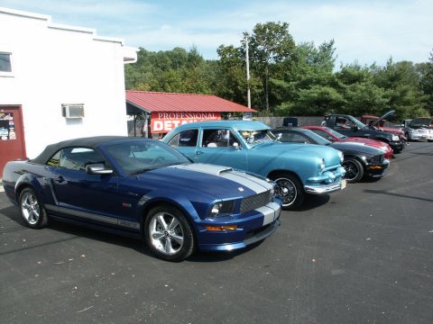 2001 Mercury Grand Marquis - A blue convertible Mustang with silver racing stripes is parked in front of other vehicles at an outdoor car show.